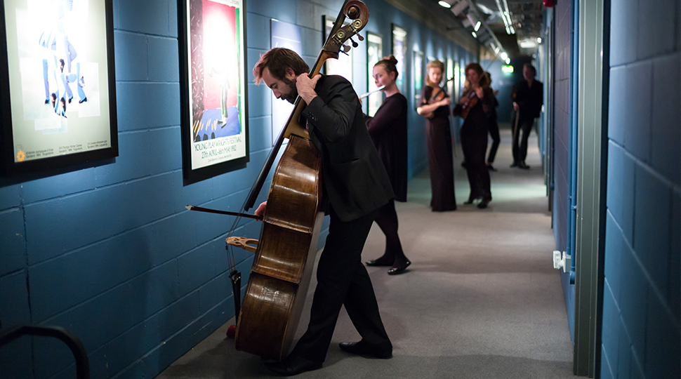 Aurora Orchestra players backstage, musician standing at the forefront with double-bass in focus