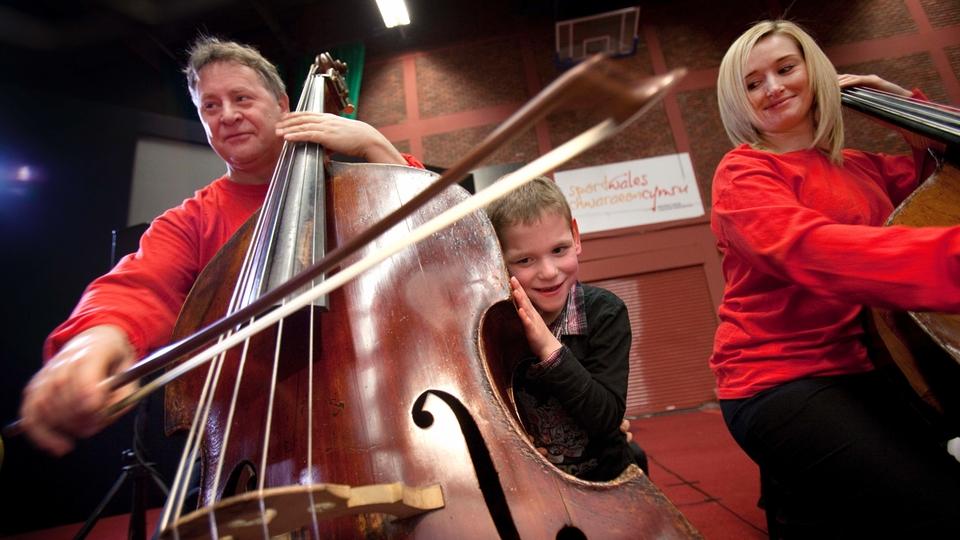 A child presses his ear against a double bass as a musician plays