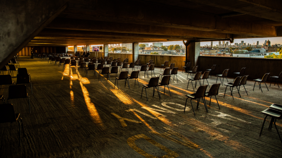 Inside a car park with many chairs, positioned like a theatre audience, and no cars.