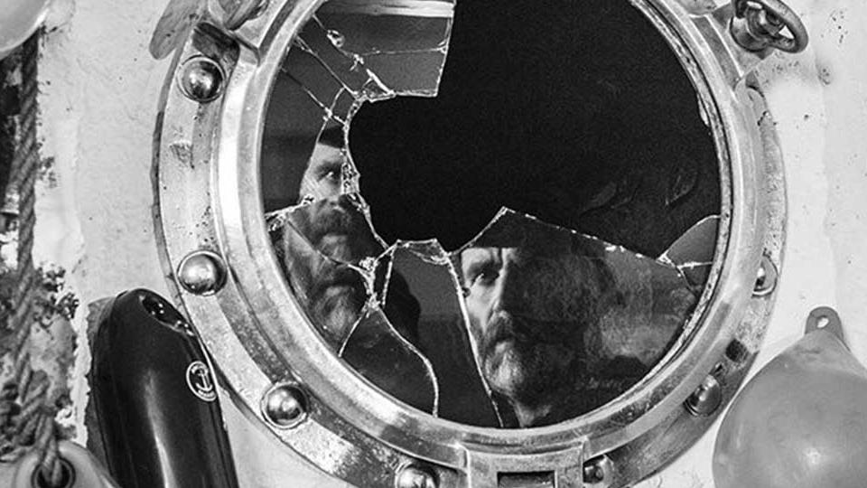 Man's reflection shattered in broken porthole - a still from Bait film